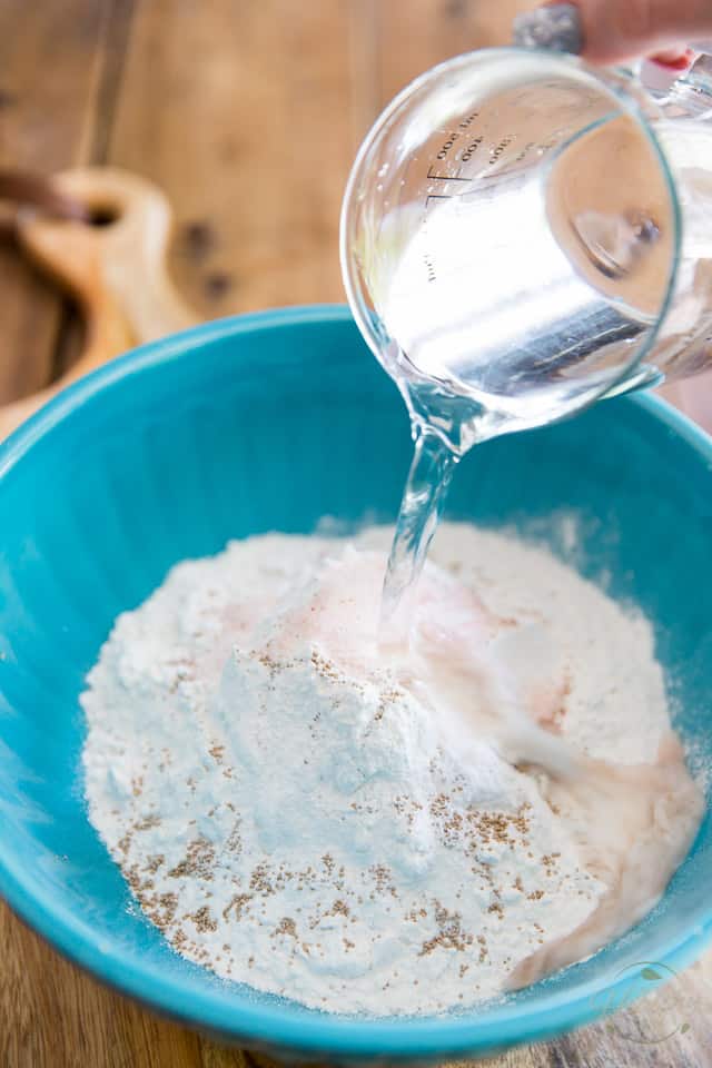 Water is being poured into a blue bowl containing flour, salt and active dry yeast