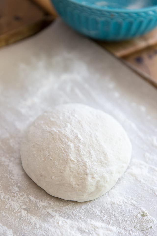 A ball of uncooked dough sitting on a piece of floured parchment paper