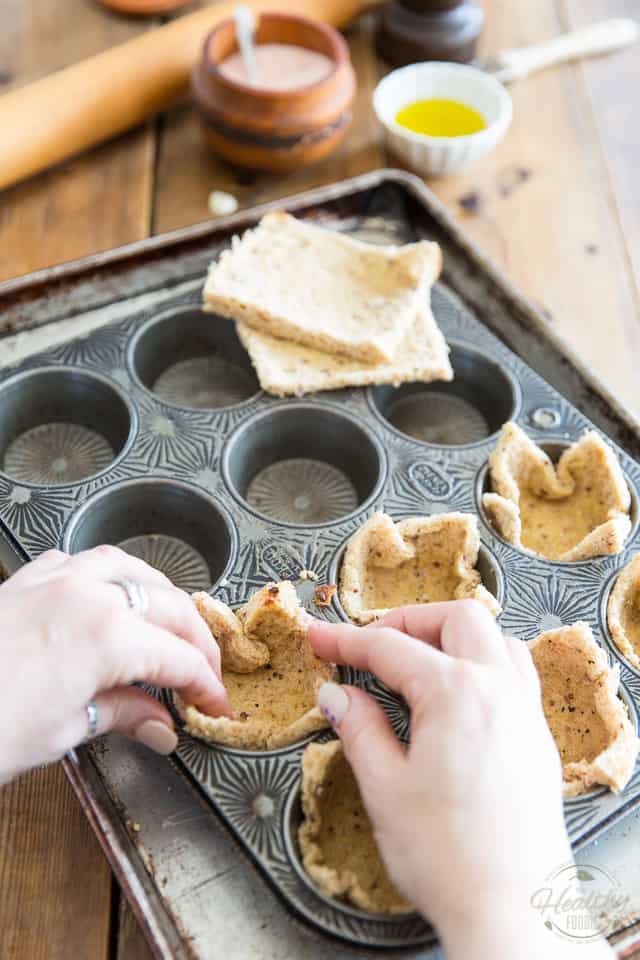 Flattened pieces of bread are being pushed into a muffin tin to form toast cups