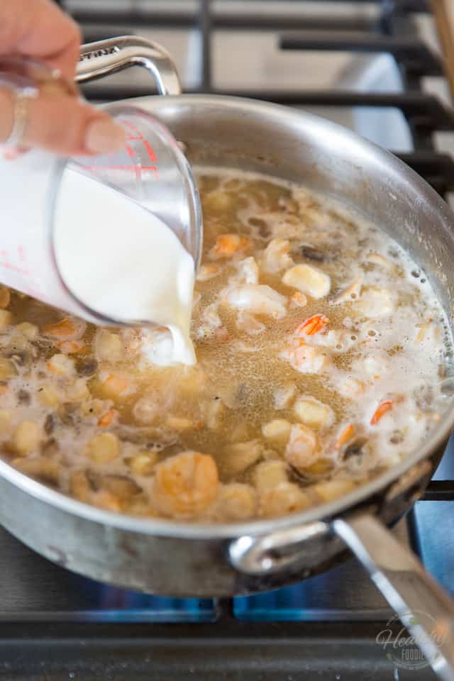 Chicken broth is being poured into a pan containing mushrooms shrimps and scallops