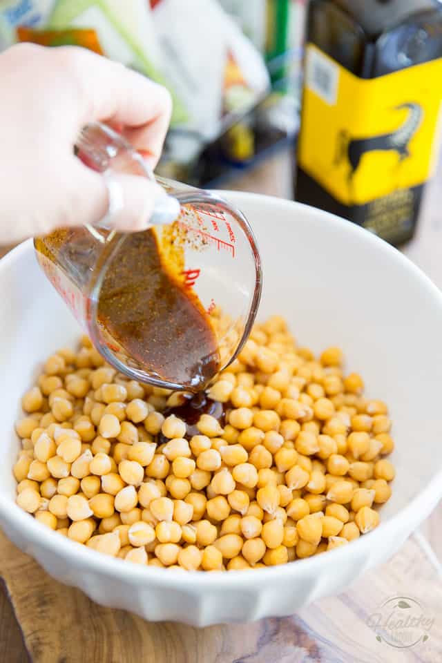 Tex Mex seasoning is being poured into a white bowl containing cooked chickpeas