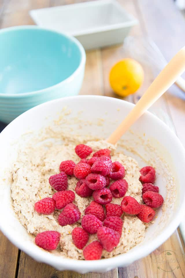 Overhead view of a white ceramic bowl containing cake batter and fresh raspberries