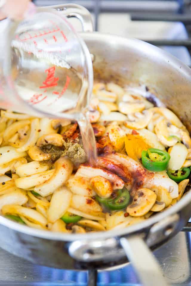 Wine being poured over onions, mushrooms and jalapeno peppers cooking in a stainless steel saute pan