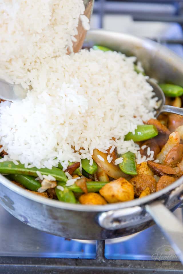 Rice is being added to a pan containing meat and veggies