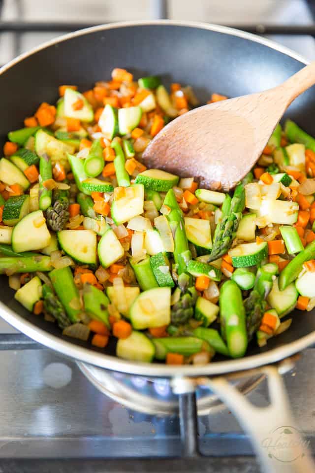 Onions, diced carrots, zucchini and asparagus cooking in a non-stick skillet