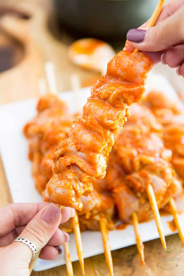 Pieces of raw chicken covered in buffalo sauce threaded onto a wooden skewer