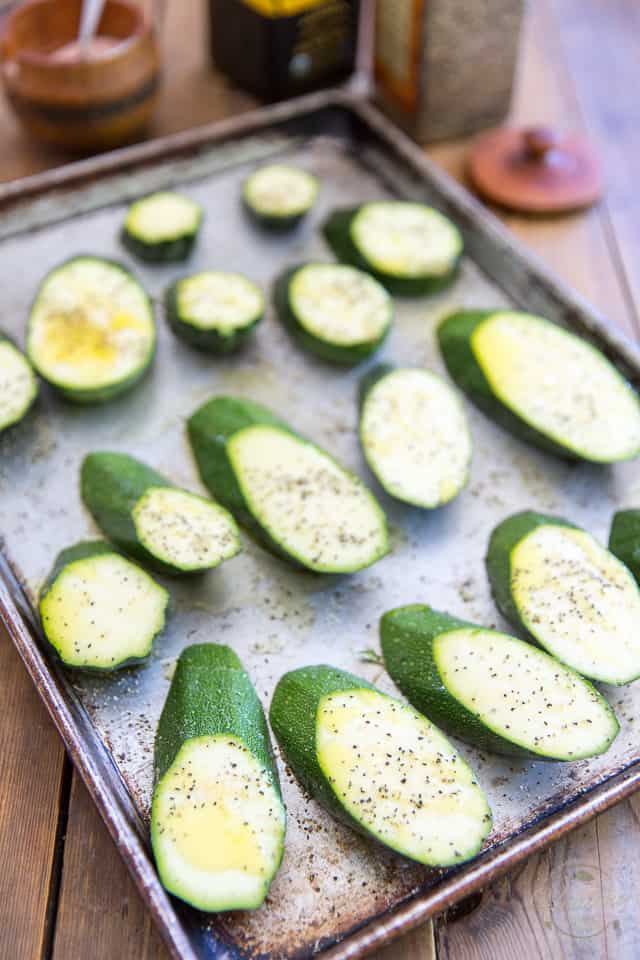 Sliced zucchini on a baking sheet, seasoned with salt and peper