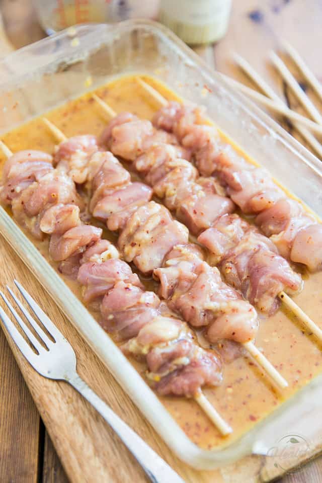 Raw chicken skewers marinating in a glass baking pan