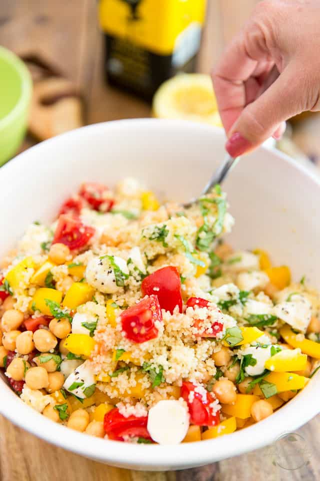 Salad containing chickpeas, raw veggies and couscous getting tossed with large spoon