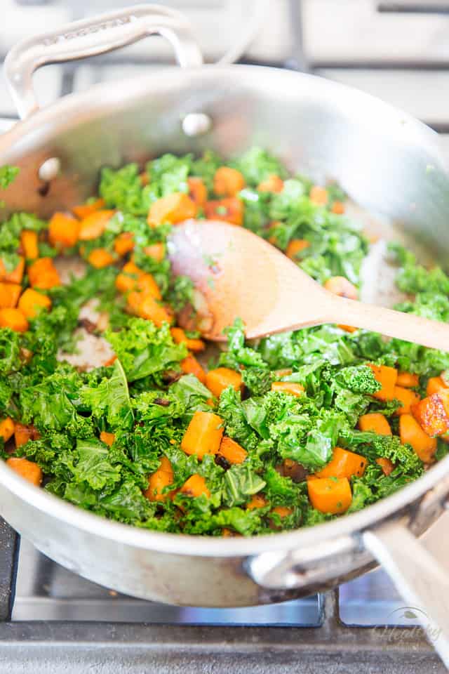 Chopped Kale and cubes of sweet potatoes cooking in a stainless steel saute pan