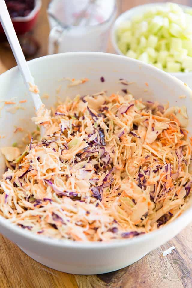 Coleslaw getting tossed in white ceramic bowl