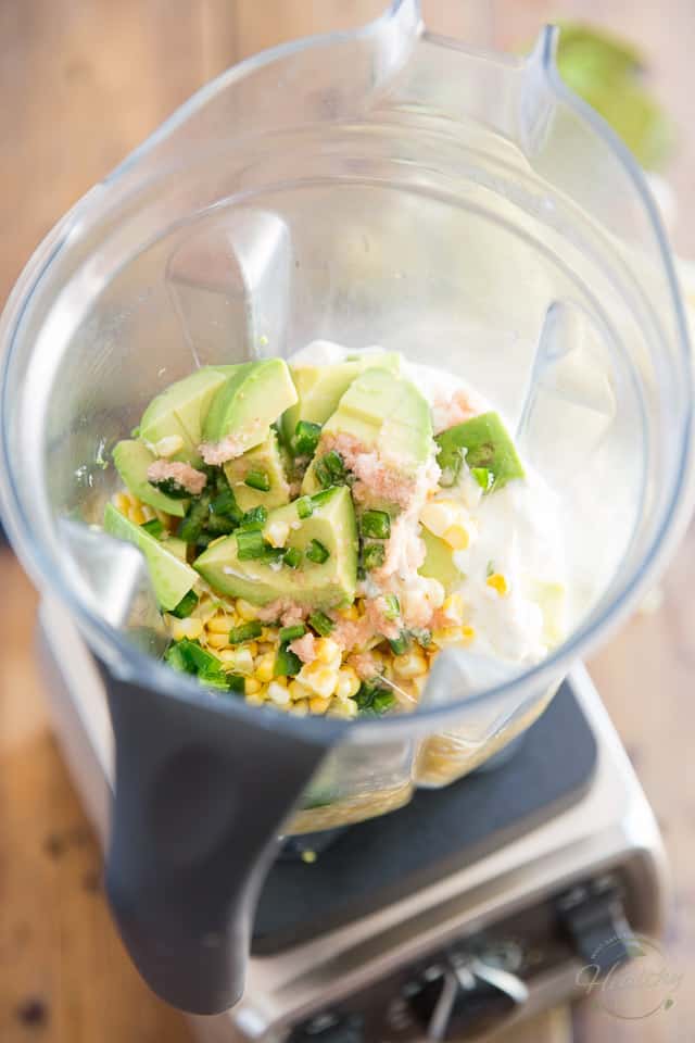 Corn Kernels, avocado, jalapeno peppers, salt and yogurt in the container of a high speed blender, viewed from above