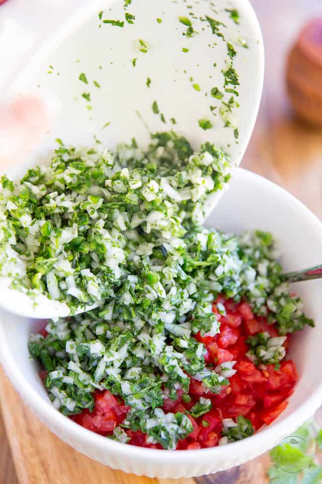 Chopped onions, jalapenos, cilantro, lime juice and salt are being added to finely diced tomatoes