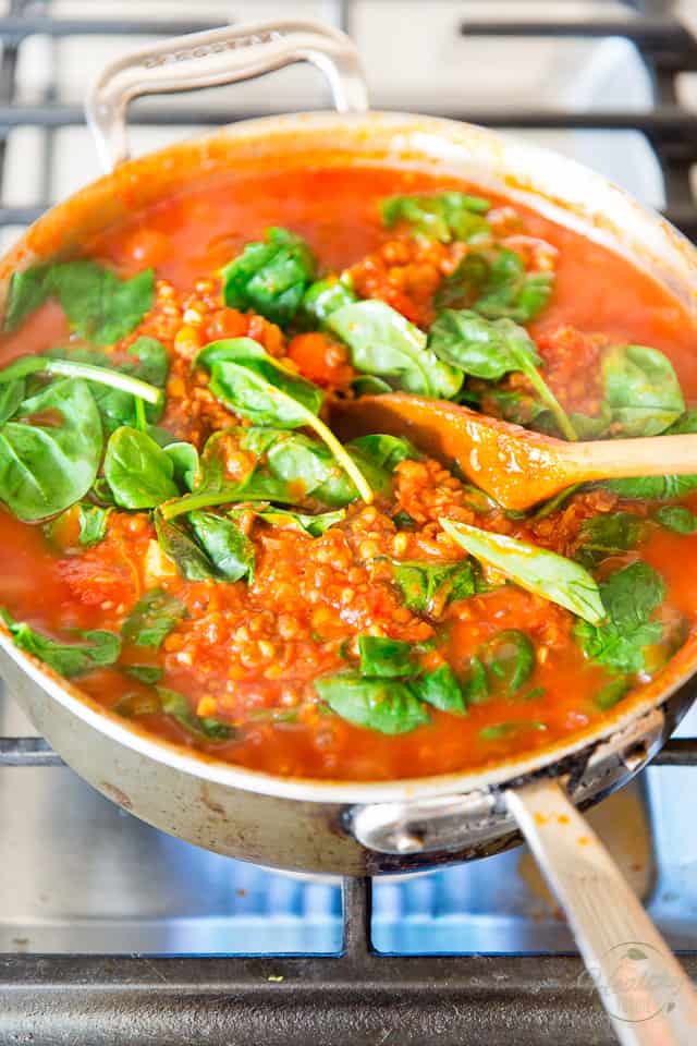Adding spinach to tomato sauce simmering in saute pan