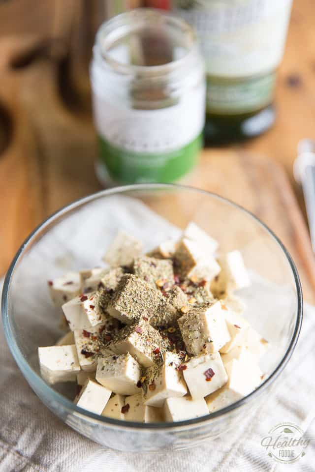 Cubed tofu in a glass bowl covered with dried herbs and spices 